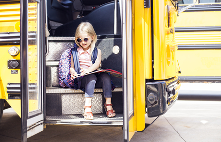 Schoolgirl sitting in school bus and reading the book. Back to school or education conceptの写真素材