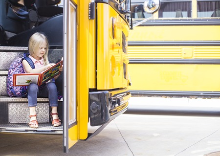 Schoolgirl sitting in school bus and reading the book. Back to school or education conceptの写真素材