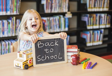Cheerful girl holding chalkboard with words. Back to school in the libraryの写真素材