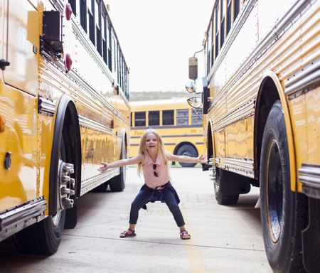 Happy little girl with backpack next to school bus. Back to school concept