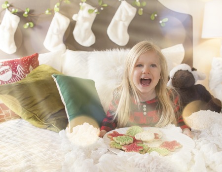 Joyful girl in bed holding cookies for santa claus - Christmas timeの写真素材