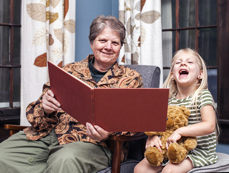 Grandmother reading night story to her granddaughter at homeの写真素材