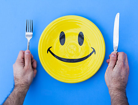 Male hands with cutlery and plate with smiling face on blue backgroundの写真素材