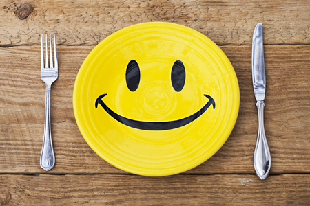 Yellow plate with smile and cutlery on wooden tableの写真素材