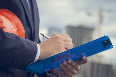 Close-up of worker inspector holding clipboard on the background of constructionの写真素材