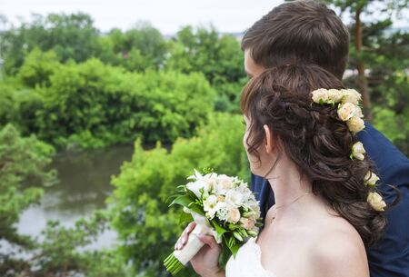 Rear view of young married couple looking together at view. Bride standing at broom and holding...