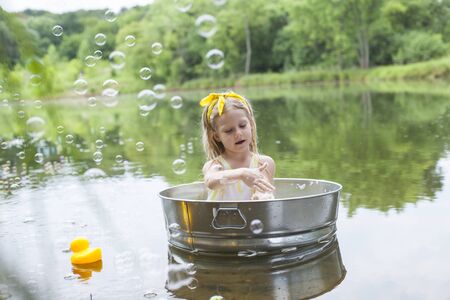 Concentrated little girl sitting in tub and bathing outside. Child washing arms at lake. Hygiene, summer, childhoodの写真素材