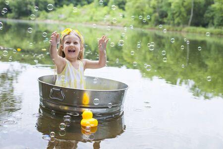 Excited little girl enjoying soap sud at lake. Happy kid sitting in metal tub in summer. Summer, childhood, vacationsの写真素材