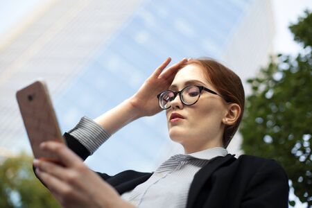 Close-up of serious young businesswoman reading text message. Portrait of female manager looking at smartphone and touching head. Businesswoman having problemの写真素材