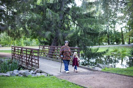 Happy grandmother walking with her granddaughter in park. Senior woman and little girl walking on bridge outdoorsの写真素材