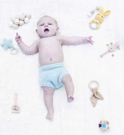 Portrait of displeased little baby lying on blanket with toys. Above view of baby boy wearing blue diaper resting in bed. Newborn child, childhood, healthy childの写真素材