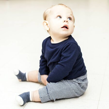 Concentrated little boy sitting and looking away. Baby boy wearing blue sweater and striped pants. Newborn childhood, childhoodの写真素材