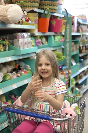 Eau Claire, WI, USA - October 20, 2019. Smiling little girl sitting in shopping cart at toy aisleのeditorial素材