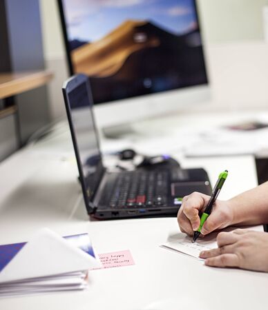 Close-up of male hands writing note at workplace. Hands of businessman sitting at table with laptop and envelopes. Secretary or receptionist workingの写真素材