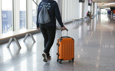 Close-up of a woman passenger walking with orange suitcase and drawstring bag along terminal hall. Tourist arriving or leaving. Travelling people, tourism, airplane tripの写真素材