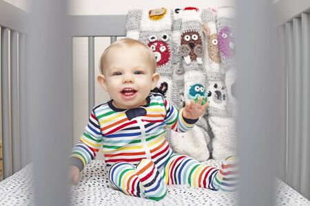 Portrait of happy baby boy sitting in cradle and looking at camera. Little kid wearing jumpsuit in crib. Childhood, childcareの写真素材