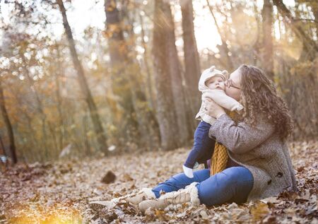 Portrait of happy young woman sitting on foliage kissing her son. Mother wearing glasses and coat...