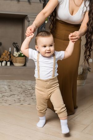 Portrait of little boy learning to walk with his mother. Baby son making first steps with help of mom. Baby steps, childcare, childhoodの写真素材