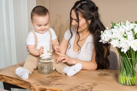 Portrait of happy young mother playing with baby son. Little boy sitting on wooden table playing with jar. Childcare, family, motherhoodの写真素材