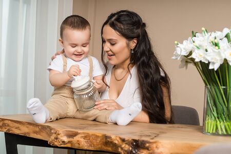 Portrait of curious baby boy playing with sugar jar with mother. Little child sitting on wooden table, young woman playing with him. Childcare, family, motherhoodの写真素材
