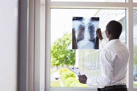 Doctor examining chest x-ray in clinic. Rear view of African American general practitioner standing...