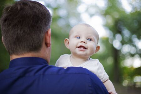 Cute laughing baby walking with father. Rear view of man carrying little son. Childhood and fatherhood conceptの写真素材