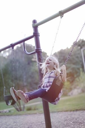Portrait of happy little girl riding a swing. Child playing in playground. Childhood conceptの写真素材