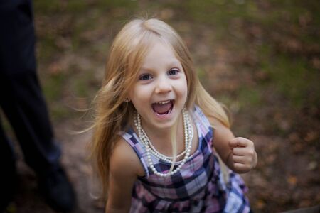 Portrait of excited little girl walking outdoors. Child wearing dress and necklaces. Childhood conceptの写真素材