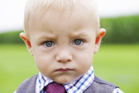 Portrait of frowning little boy looking at camera. Close-up of serious child wearing formal suit. Little businessman, bossy childの写真素材