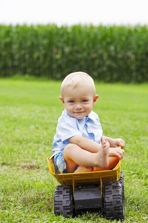 Portrait of smiling little boy sitting in toy truck outdoors. Cute toddler boy wearing shirt posing in park. Childhood, summerの写真素材