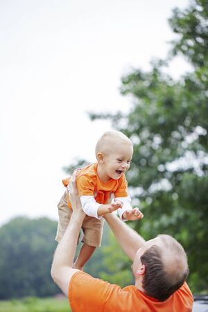 Happy father having fun with little son outdoors. Portrait of excited toddler boy laughing in hands of mid adult man. Family, parenthood, fatherhoodの写真素材