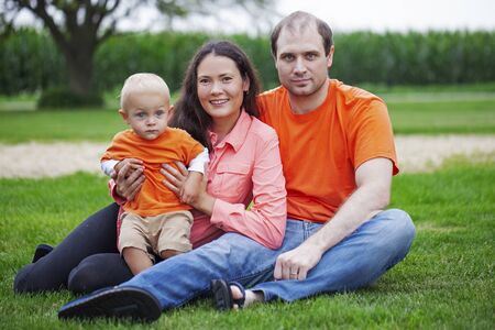 Portrait of happy family with little son sitting on grass. Mid adult couple with toddler boy spending time in park in summertime. Family, parenthood, relationshipsの写真素材