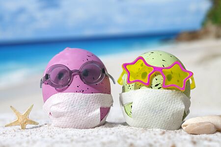 Easter eggs with faces mask at beach. Travel concept. Protection from corona virusの写真素材