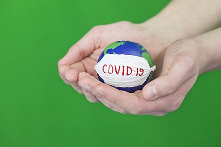 Stop corona virus. Conceptual photo of male hands holding globe with face mask on it isolated on green backgroundの写真素材