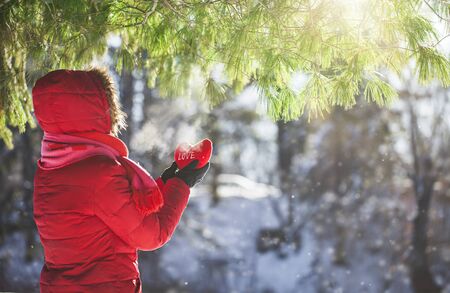Woman in red winter jacket holding heart with word love in snowy weatherの写真素材