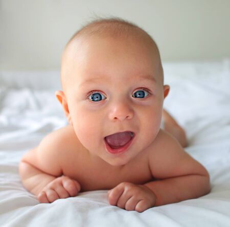 Happy cute baby boy on bed at homeの写真素材