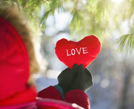 Woman in red winter jacket holding heart with word love in snowy weatherの写真素材