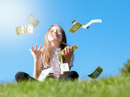 Portrait of happy girl sitting on grass catching moneyの写真素材