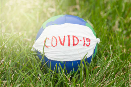 Earth day. Stop corona virus. Conceptual photo of globe with face mask on green grassの写真素材