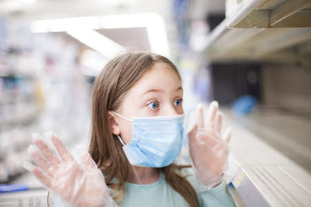 Unhealthy girl in medical mask looking or choosing medicine in pharmacy during pandemic corona virusの写真素材
