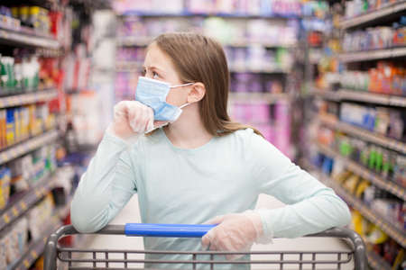 Unhealthy girl in medical mask looking or choosing medicine in pharmacy during pandemic corona virusの写真素材