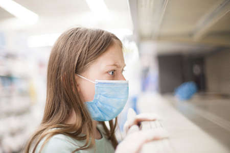 Unhealthy girl in medical mask looking or choosing medicine in pharmacy during pandemic corona virusの写真素材