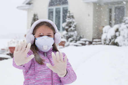 Conceptual photo of girl with faces and in medical gloves showing sign stop next to his home while winter timeの写真素材