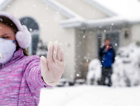 Conceptual photo of girl with faces and in medical gloves showing sign stop next to his home while winter timeの写真素材