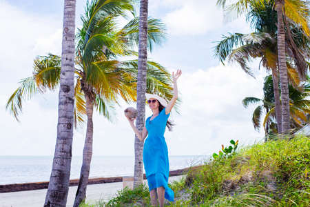 Happy woman holding the coconut next to the palms on the islandの写真素材