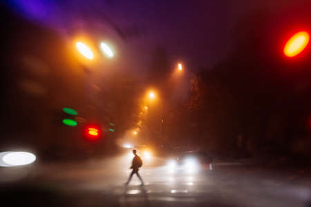 Pedestrian crossing the street during evening fogの写真素材