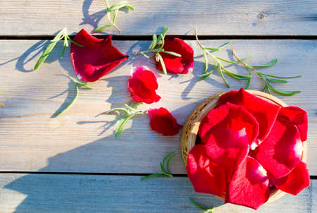 Petals of red roses in a basket on a wooden tableの写真素材