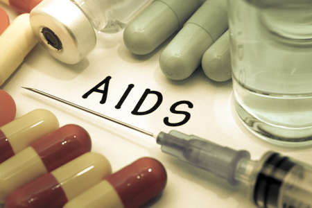 Aids - diagnosis written on a white piece of paper. Syringe and vaccine with drugs.の写真素材