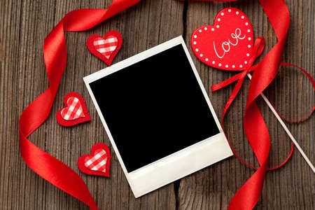 Empty polaroid photo frame with red hearts and ribbons for valentine's day on wooden backgroundの写真素材