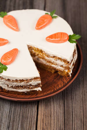 Sliced gourmet carrot sponge cake with icing cream and little orange carrots on vintage plate on...